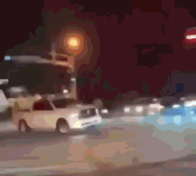 a blurred image of a street at night with a white truck in the foreground