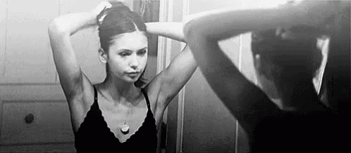 a woman in a black bra is looking at herself in the mirror .