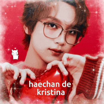 a young man with glasses is holding a red heart with the words haechan de kristina written on it