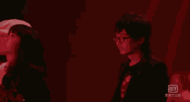 a man wearing glasses stands in a dark room with an ioiyi logo on the bottom left