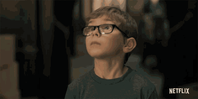 a young boy wearing glasses looks up at the sky with a netflix logo in the background
