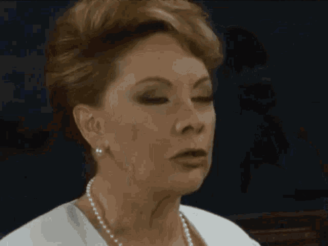a woman wearing pearls and a white shirt is making a funny face .