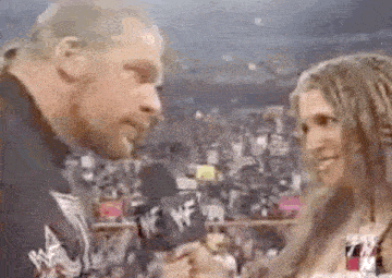 a man and a woman are talking to each other in front of a crowd in a wrestling ring .