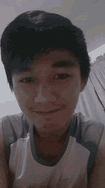 a young man wearing a grey and white tank top smiles