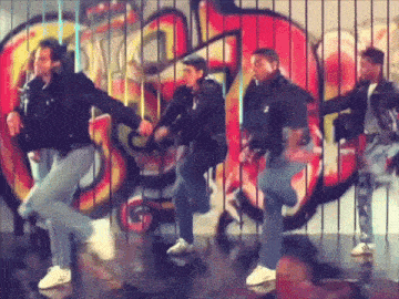 a group of men are dancing in front of a wall with graffiti