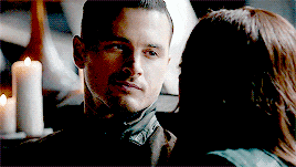 a man and a woman are looking at each other in a dark room with candles in the background