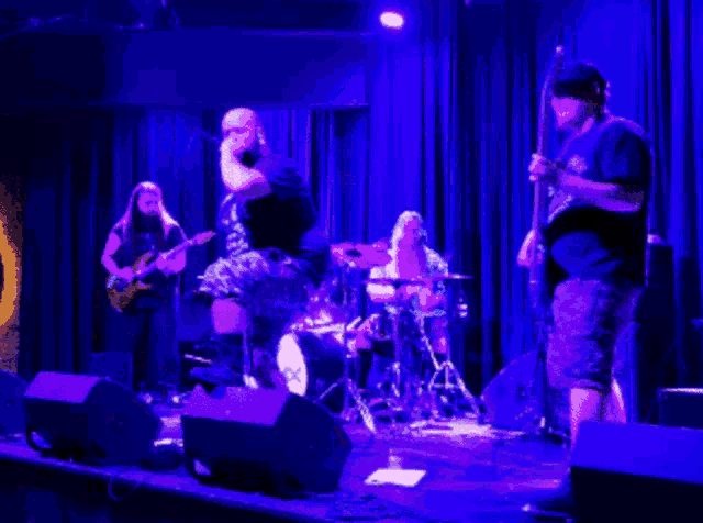 a man playing a guitar on a stage with a drummer and a woman playing a guitar