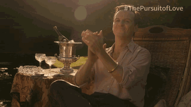 a man applauds in front of a table with a bucket of ice and a bottle of champagne