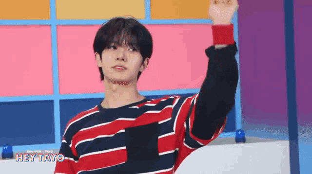a young man wearing a red , white and blue striped shirt is raising his hand .