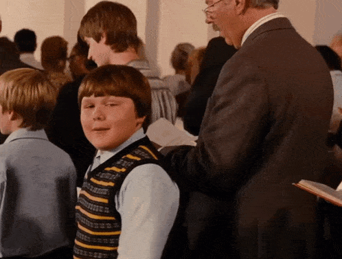 a boy wearing a striped vest stands in a crowd of people
