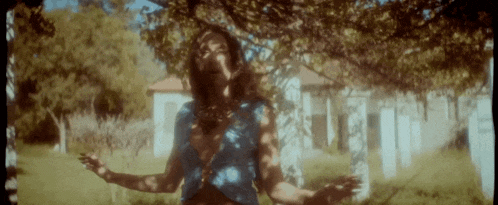 a woman in a blue top is standing in a field with her arms outstretched .
