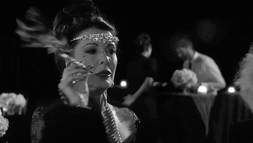 a woman wearing a headband and pearls is smoking a cigarette .