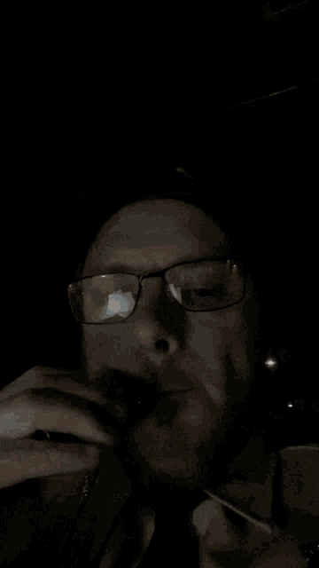 a man with glasses and a beard is blowing smoke into his mouth