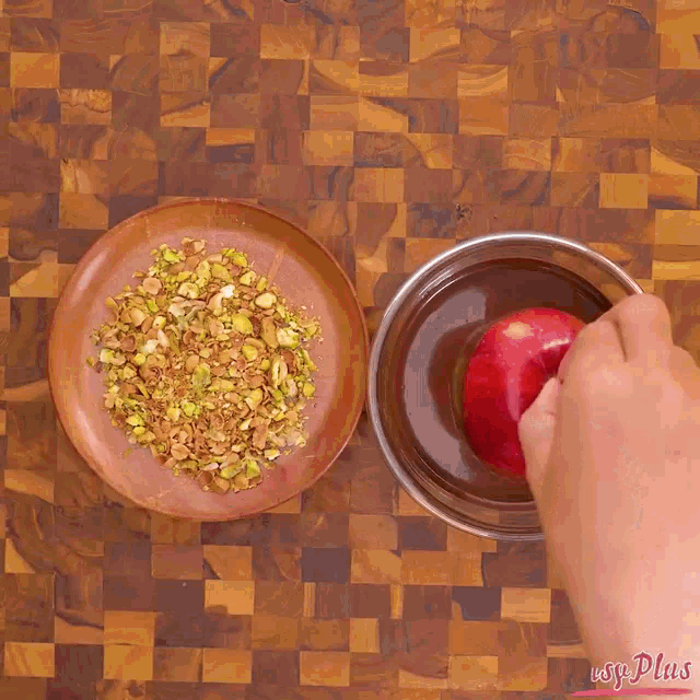 a person dipping a red apple in chocolate and nuts