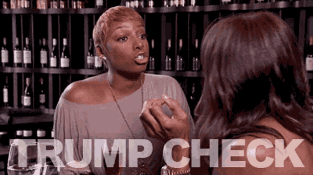 two women are talking in front of a shelf of wine bottles and the words trump check are visible