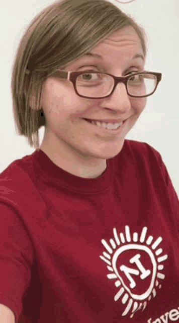 a woman wearing glasses and a red shirt with the letter n on it smiles