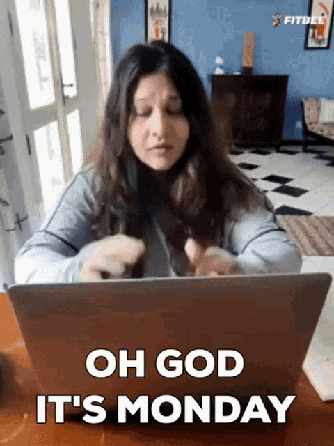 a woman is sitting in front of a laptop with the words oh god it 's monday on the screen