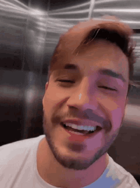 a man with a beard is smiling with his eyes closed while wearing a white shirt .