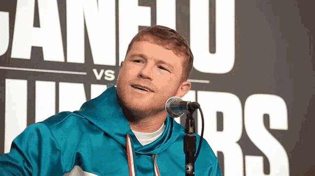 a man in a blue jacket stands in front of a microphone in front of a sign that says vs juniors