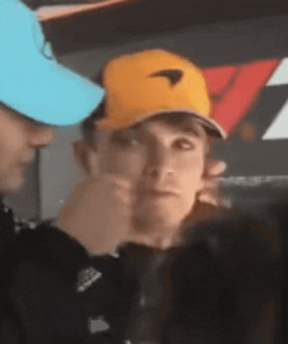 a man wearing a yellow hat is making a funny face while another man wearing a blue hat looks on .