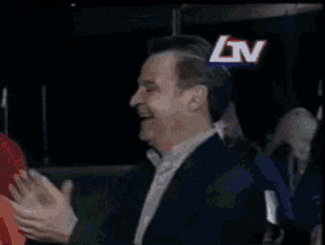 a man applauds in front of a sign that says lv on it