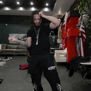 a man with dreadlocks is dancing in a living room in front of a couch