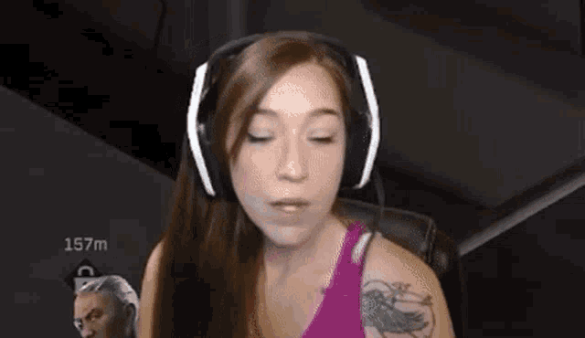 a woman wearing headphones with a microphone is sitting in a chair with 157m in the background