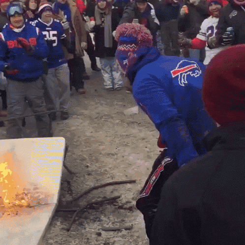 a man wearing a blue buffalo bills jersey is standing in front of a fire