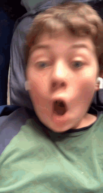 a young boy is making a surprised face while wearing a green shirt