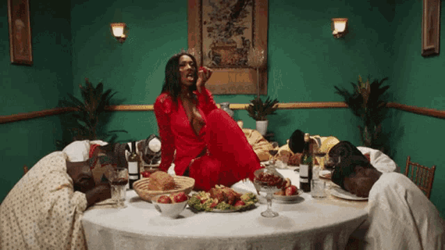 a woman in a red dress sits at a table full of food and wine
