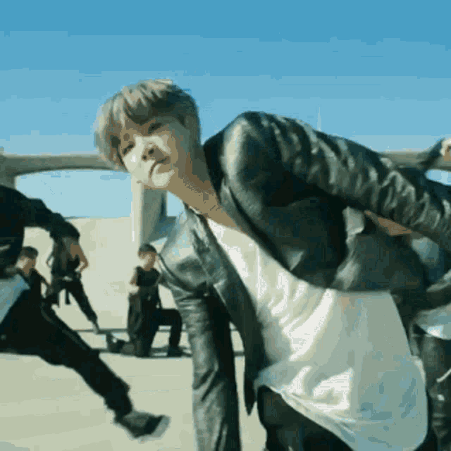 a man in a black leather jacket is dancing in front of a blue sky