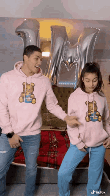 a man and a woman wearing matching pink hoodies with teddy bears on them
