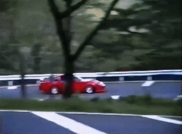 a red car is driving down a road surrounded by trees