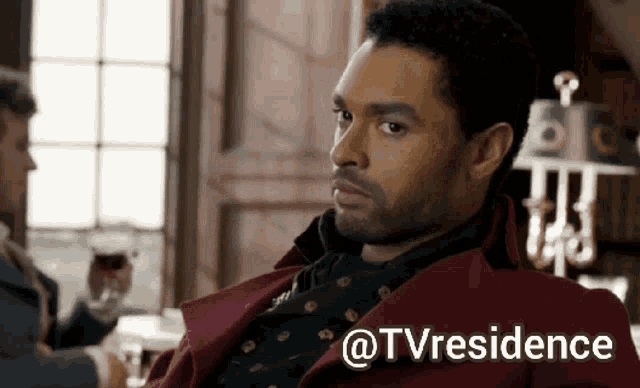 a man in a red coat is sitting in front of a window with the words " @tvresidence " on the bottom