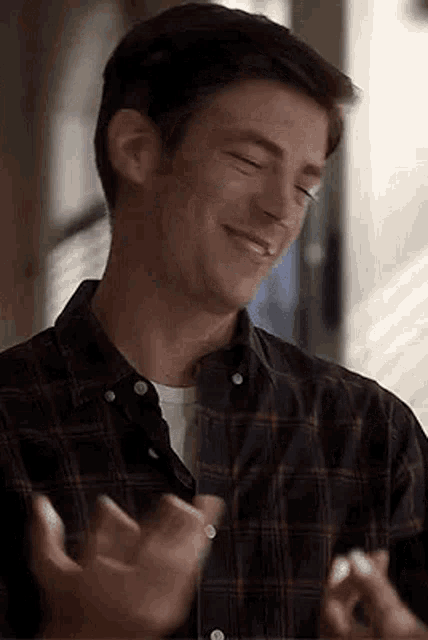 a man in a plaid shirt is smiling and clapping .