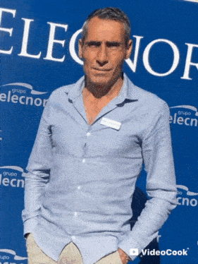 a man in a blue shirt stands in front of a sign that says grupo elecn