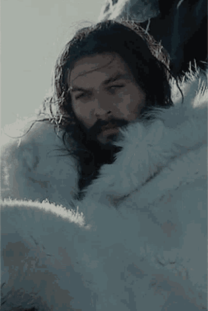 a man with long hair and a beard is laying in a white fur coat