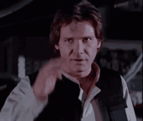 a close up of a man wearing a black vest and a white shirt pointing at the camera .