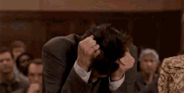a man in a suit and tie is covering his face with his hands in a courtroom .