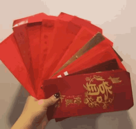 a person is holding a fan made of red envelopes with chinese writing on them .