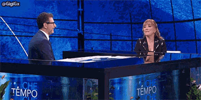 a man and a woman are sitting at a table in front of an aquarium that says che tempo