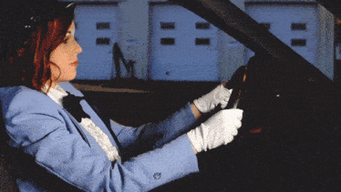 a woman wearing a blue jacket and white gloves is driving a car