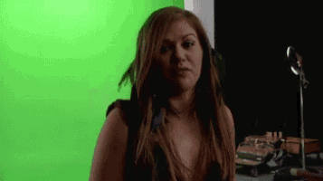 a woman is standing in front of a green screen and making a funny face .