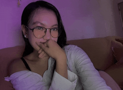 a woman wearing glasses sits on a couch with her hand on her chin