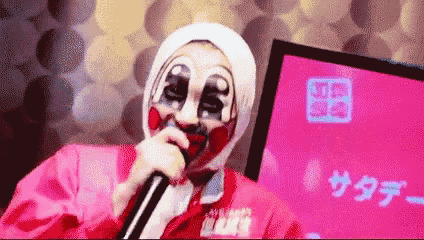 a clown is singing into a microphone with a pink background