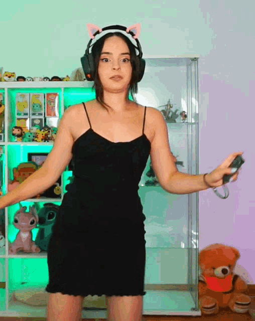 a woman in a black dress and headphones holds a remote control