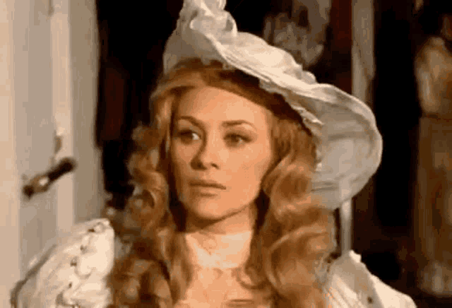 a woman wearing a white hat and a white dress is standing in front of a door .