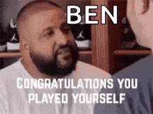 a man with a beard is talking to another man and congratulating him on playing yourself .