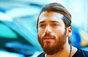 a man with a beard and ponytail is wearing a black shirt and necklace .