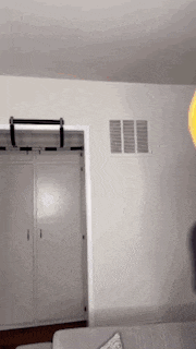 a person is standing in a living room next to a couch and a doorway .